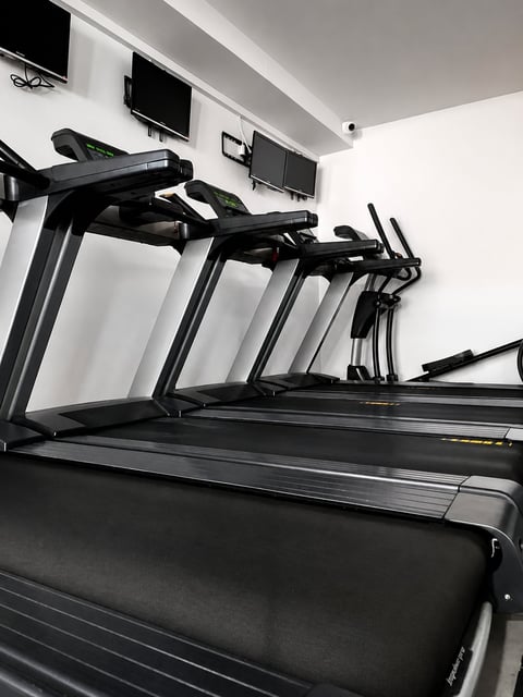 Row of modern black treadmills in a bright gym with white walls and mounted TV screens