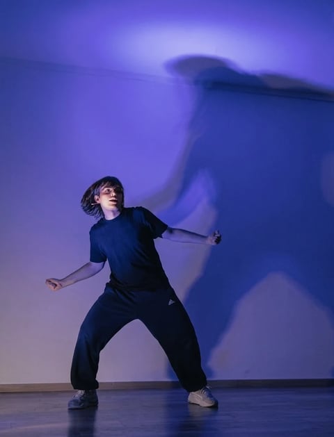 Young dancer in black outfit striking dynamic pose with large shadow projected on blue-lit background