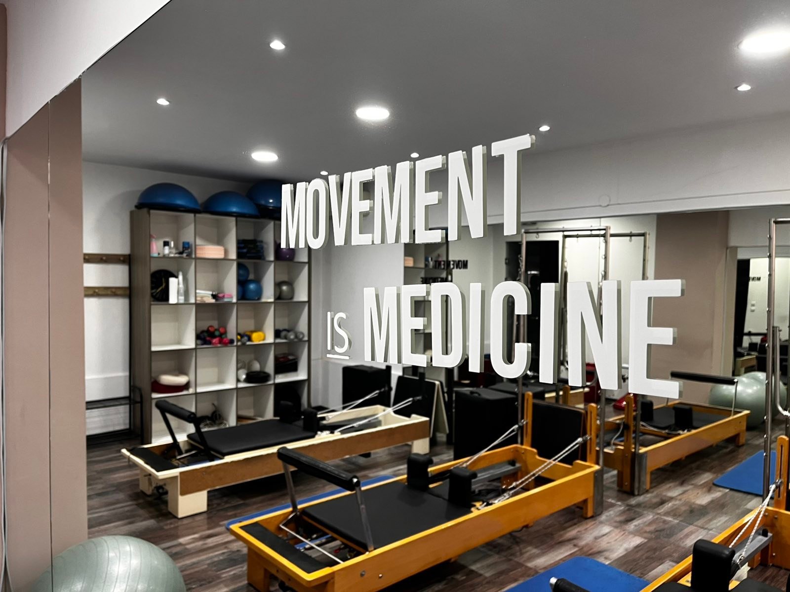 Modern physical therapy studio with Movement is Medicine wall text, wooden Pilates reformers, shelving, and recessed lighting